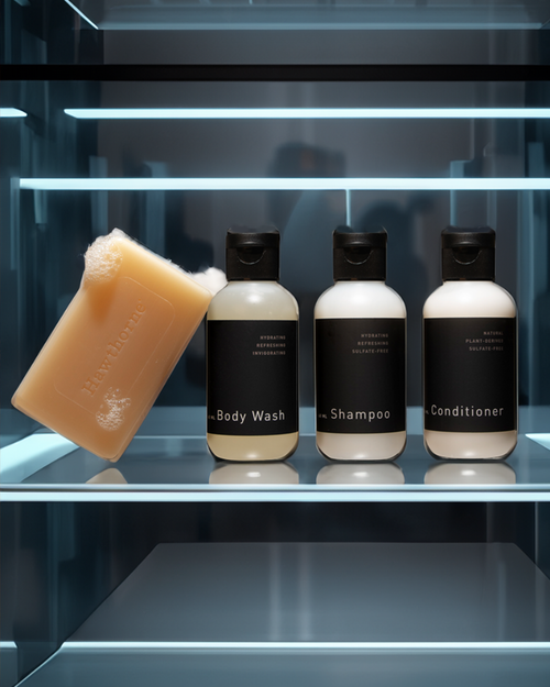 The hawthorne Travel Shower Set, featuring a bar of soap, body wash, travel shampoo, and conditioner, is displayed on a glass shelf with a modern background.